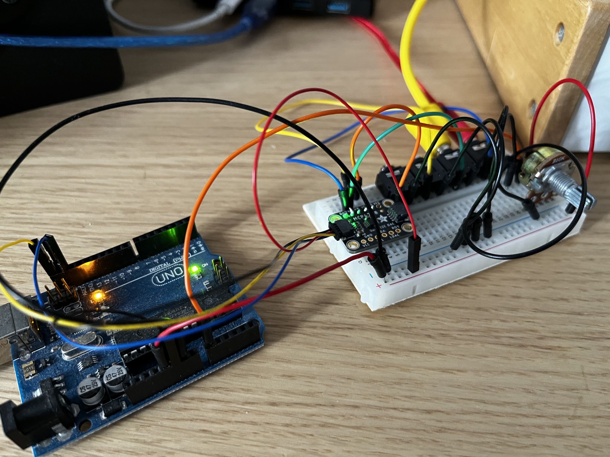 An Arduino microcontroller and a breadboard with an even smaller chip, a bunch of sockets and a rotary pot, all connected with colourful jumper leads